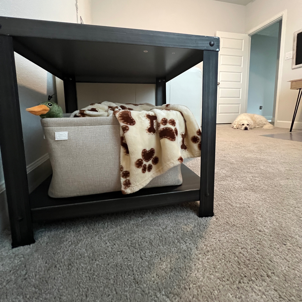 Neutral beige basket with blanket and duck toy in a room with a white dog resting calmly.